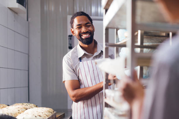 Smiling baker organizing fresh bread on shelves in bakery