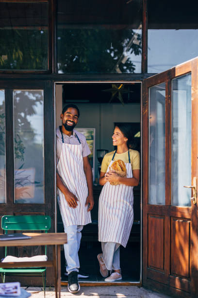 Smiling bakers standing in bakery doorway holding fresh bread